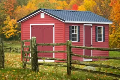 A shed in Kentucky with red vinyl siding and a metal roof on a fall day