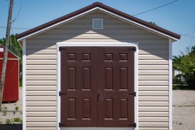 A storage shed in Tennessee with vinyl siding, brown double doors, and a brown metal roof
