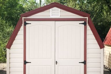 A backyard shed in Tennessee with white vinyl siding, a red metal roof, and double doors